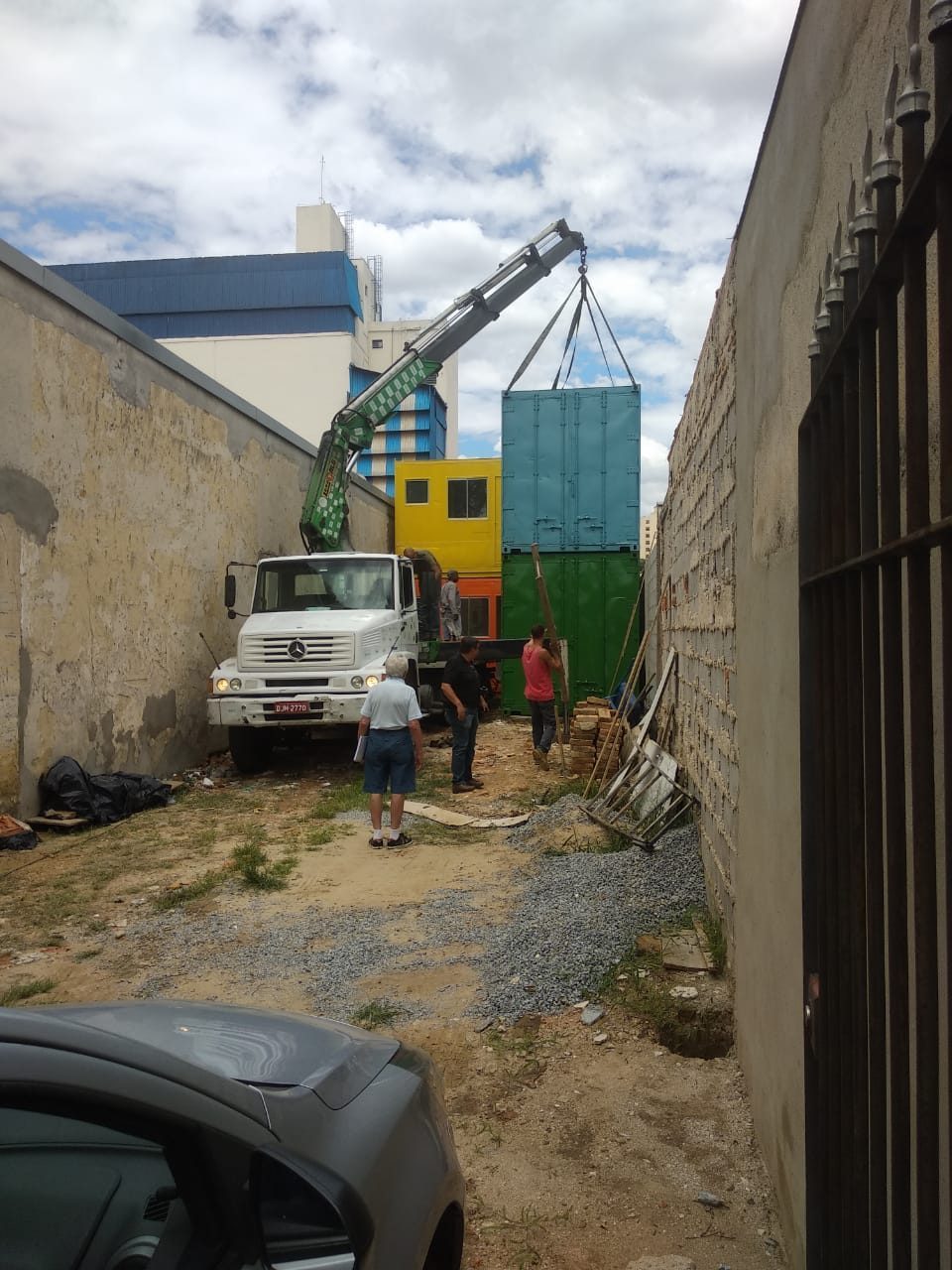 A truck-mounted crane lifting a container over the wall into the lot